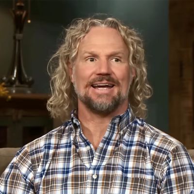 Kody has a curvy shoulder length hair and is wearing a check designed shirt.